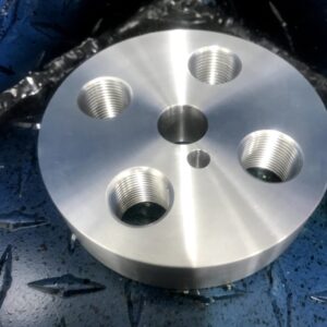 CNC machined circular steel die plate with four precision threaded ports and a central bore, manufactured by Matteson Machine Shop.